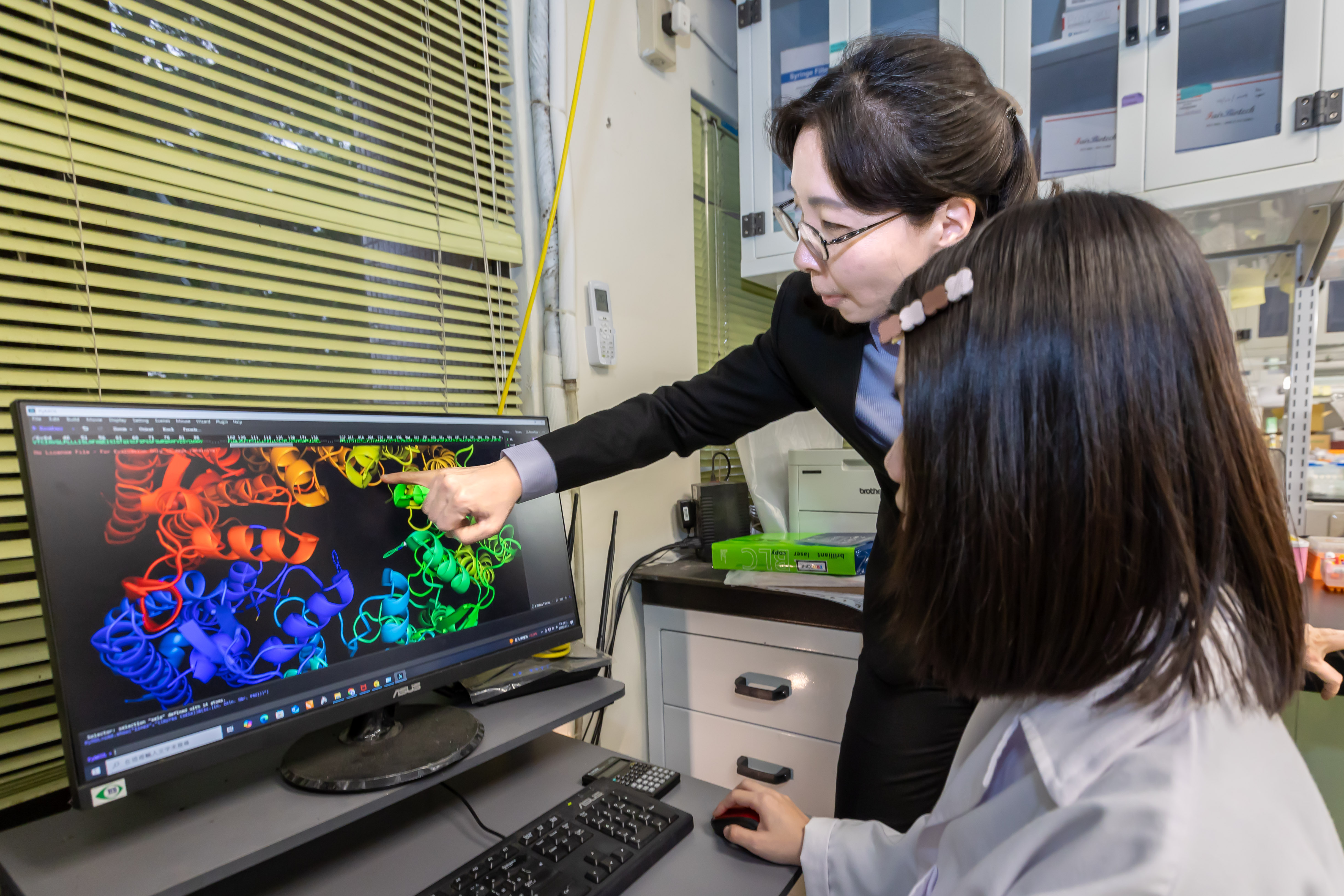 Master's student Neng-Jie Zeng (曾能杰) (left) from NTHU's Institute of Molecular Medicine uses a microscope to observe the immobilization of nematodes controlled by light.